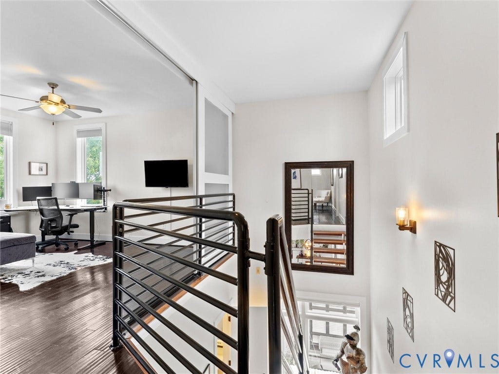 Dark wood-finish flooring, black metal horizontal bar railing, ceiling fan with integrated lighting, wall-mounted sconce lighting, and a sliding panel door