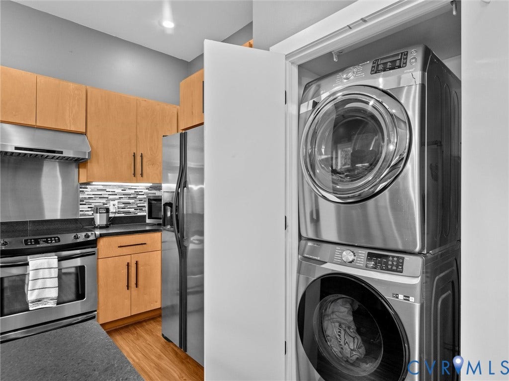 Kitchen featuring stainless steel appliances, wood-finish cabinetry, dark countertops, and a tiled backsplash