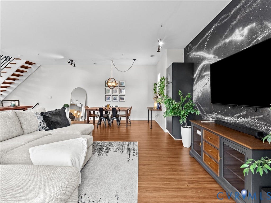 Wood-finish flooring throughout, with a striking accent wall, track lighting, and a contemporary open staircase