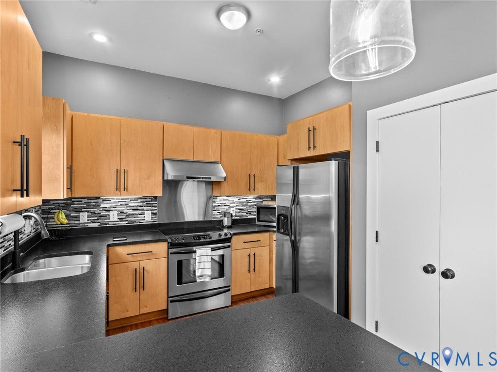 Kitchen with wood-finish cabinetry, stainless steel appliances, black countertops, and a tiled backsplash