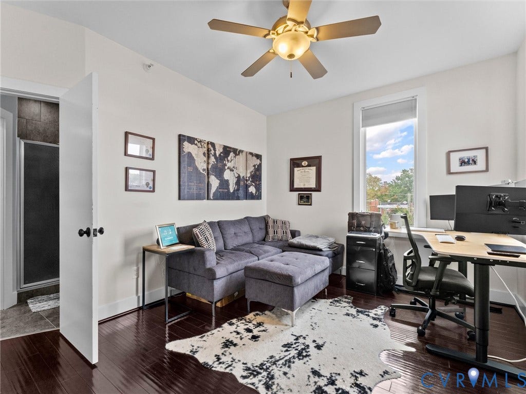 Rich wood-finish flooring, bright window, ceiling fan with integrated lighting, and a white interior door