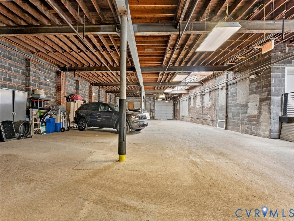 Concrete flooring, exposed wood ceiling joists, exposed brick walls, and fluorescent lighting