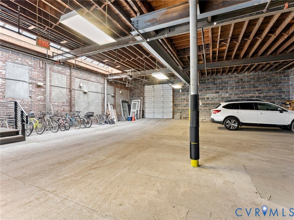 Exposed wood beam ceiling, exposed brick wall, concrete block wall, concrete flooring, and an overhead garage door
