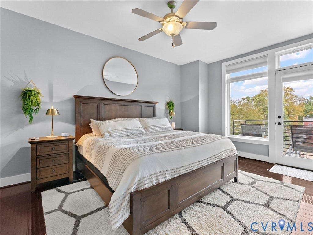 Wood-finish flooring, ceiling fan with integrated lighting, built-in nightstands, and a glass-paneled door opening to an exterior balcony