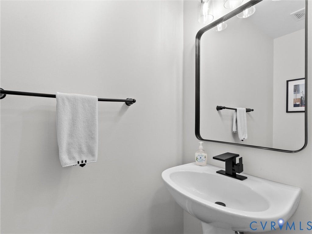 Pedestal sink with a matte black faucet, framed mirror, and modern wall-mounted light fixture