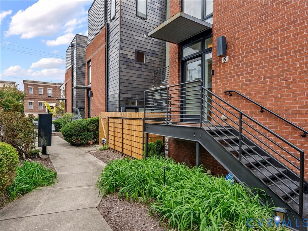 Brick facade with slate-style siding, metal staircase with railings, and established landscaping