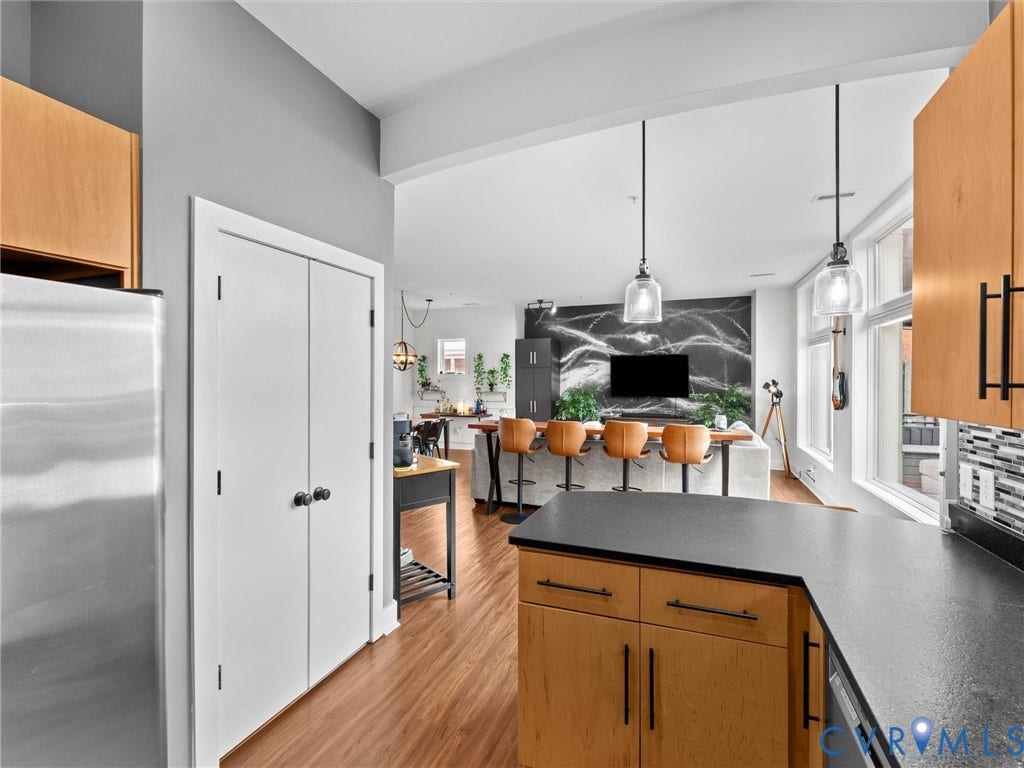 Kitchen featuring wood-finish flooring, light wood cabinetry, dark countertops, and a tile backsplash