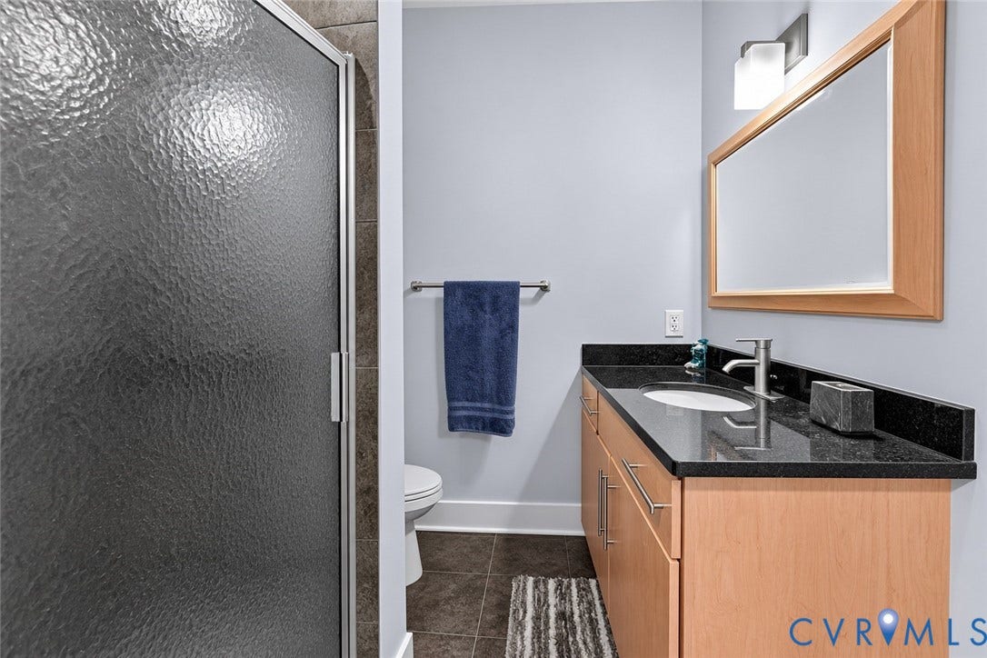 Frosted glass shower enclosure, wood-finish vanity with dark countertop, undermount sink, and wall-mounted mirror