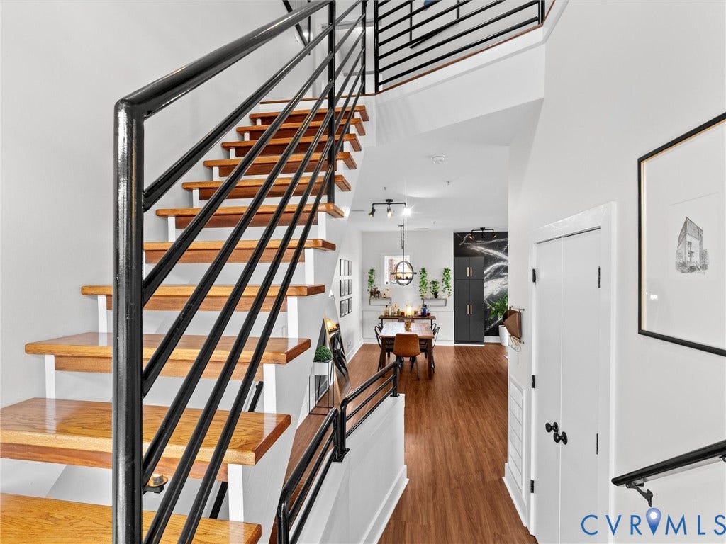Wood-finish flooring throughout, open-tread staircase with black metal railings, and white interior doors with black hardware