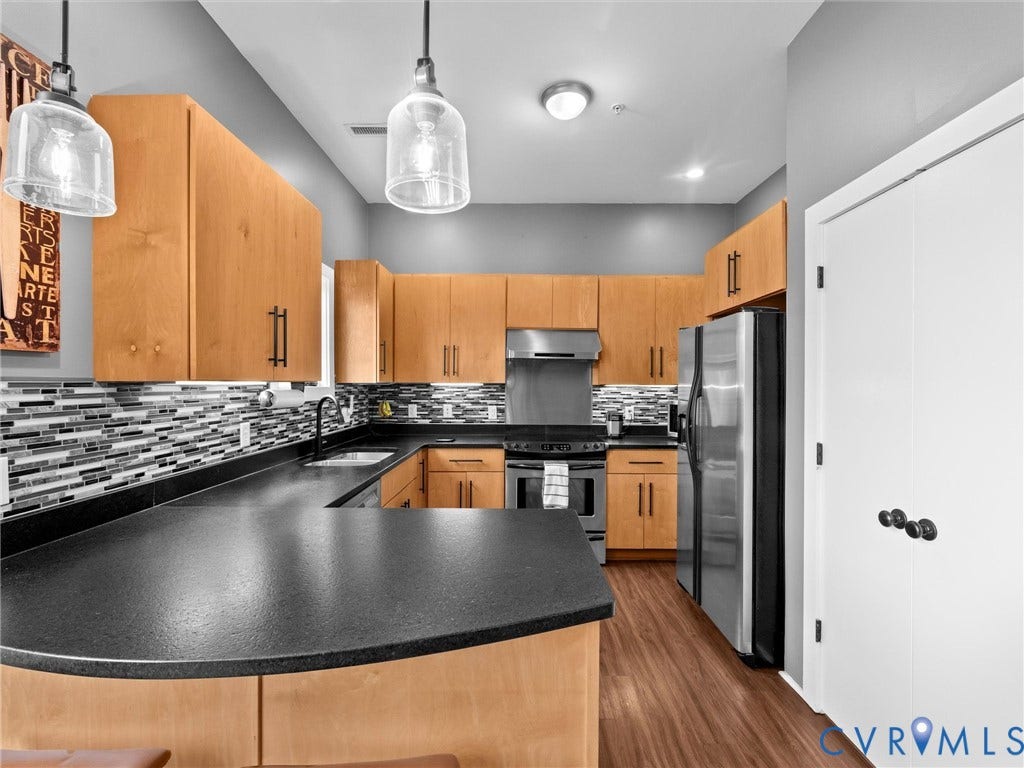 U-shaped kitchen featuring wood cabinetry, stainless steel appliances, dark countertops, a mosaic tile backsplash, and wood-finish flooring