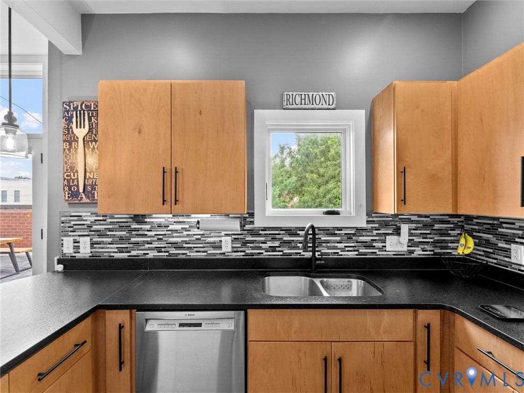 Wood-finish cabinetry with matte black hardware, black countertops, stainless steel dishwasher, and mosaic tile backsplash