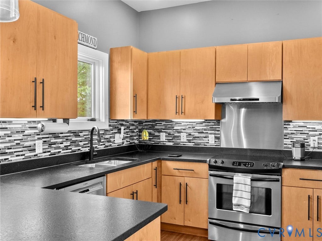 Kitchen featuring wood cabinetry, dark countertops, a mosaic tile backsplash, stainless steel appliances, and an under-mount sink