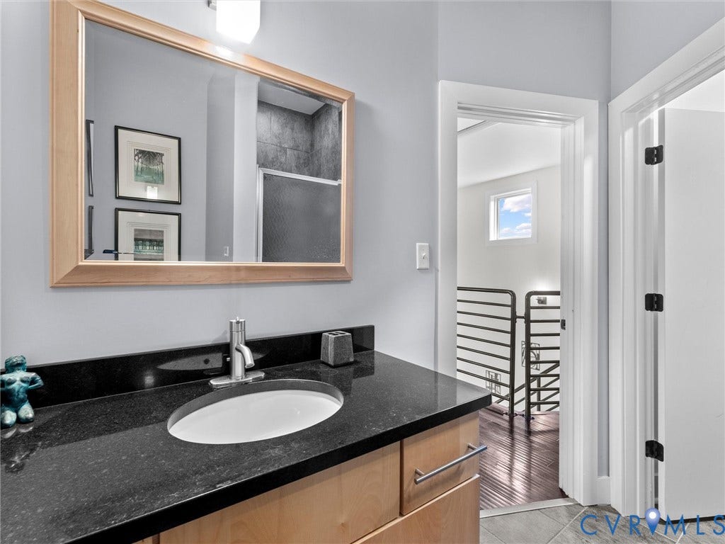 Vanity with an integrated oval sink, stone countertop, wood-finish cabinetry, and a framed mirror