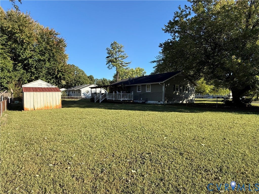 Expansive grassy area with a storage shed, a covered deck, and mature trees