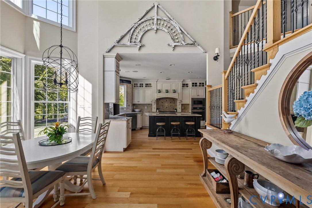 Hardwood flooring throughout, two-story windows with transom accents, a spacious kitchen featuring an island with built-in seating, and a grand staircase with wrought iron balusters
