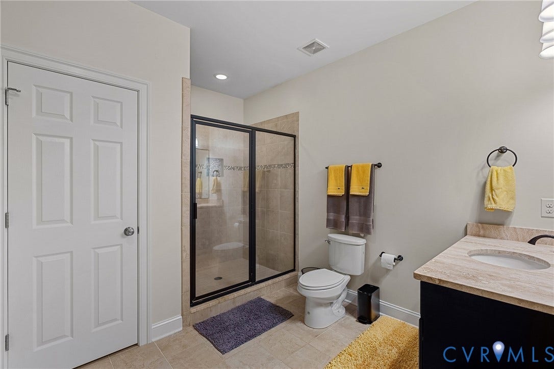 Tiled flooring, glass-enclosed shower, single vanity with countertop, wall-mounted sink faucet, and recessed lighting