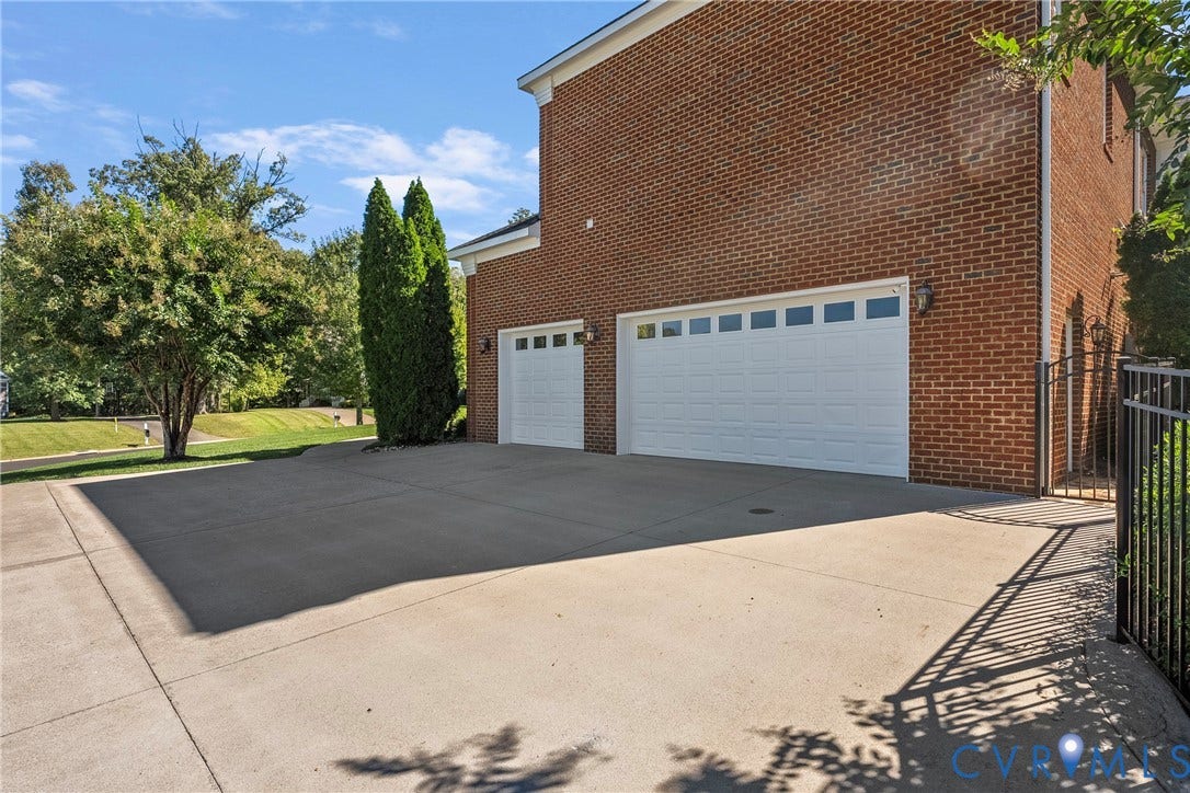 Brick exterior with two white garage doors, a concrete driveway, and a black metal fence