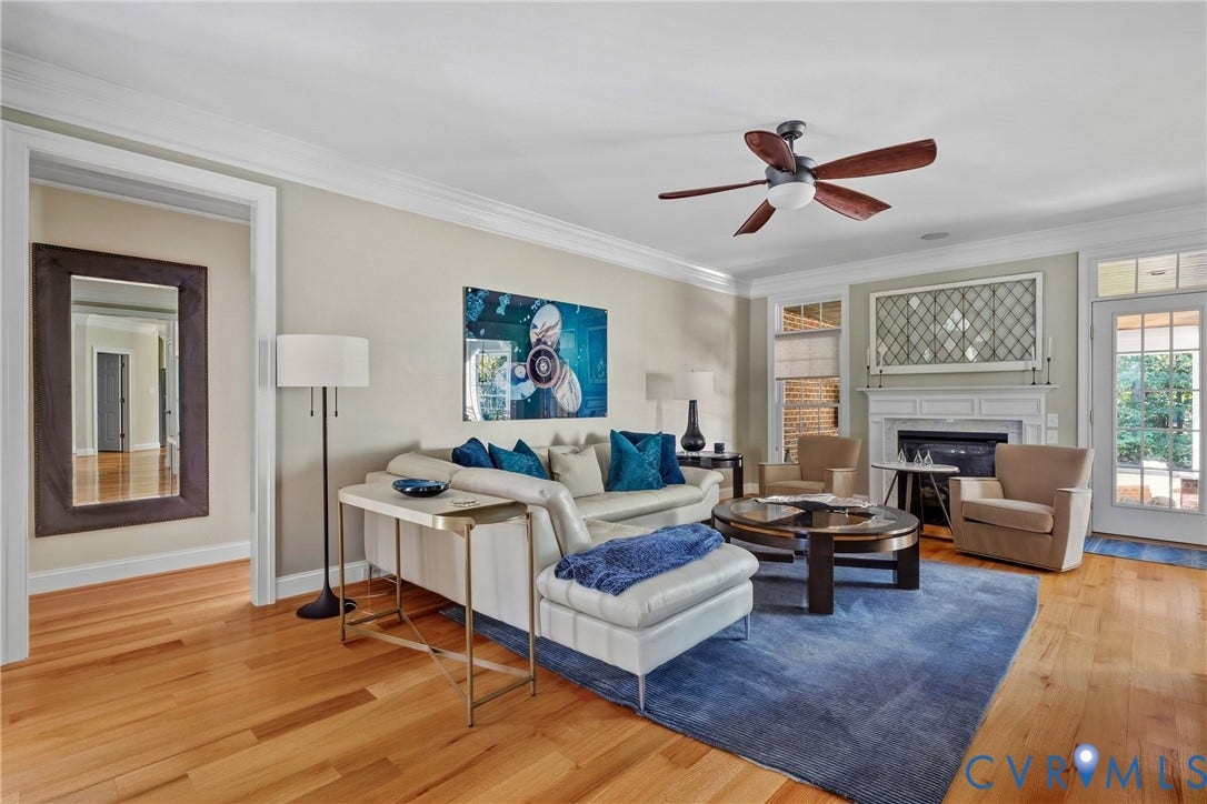 Hardwood flooring, crown molding, a ceiling fan, a white mantel, and a glass-paneled door