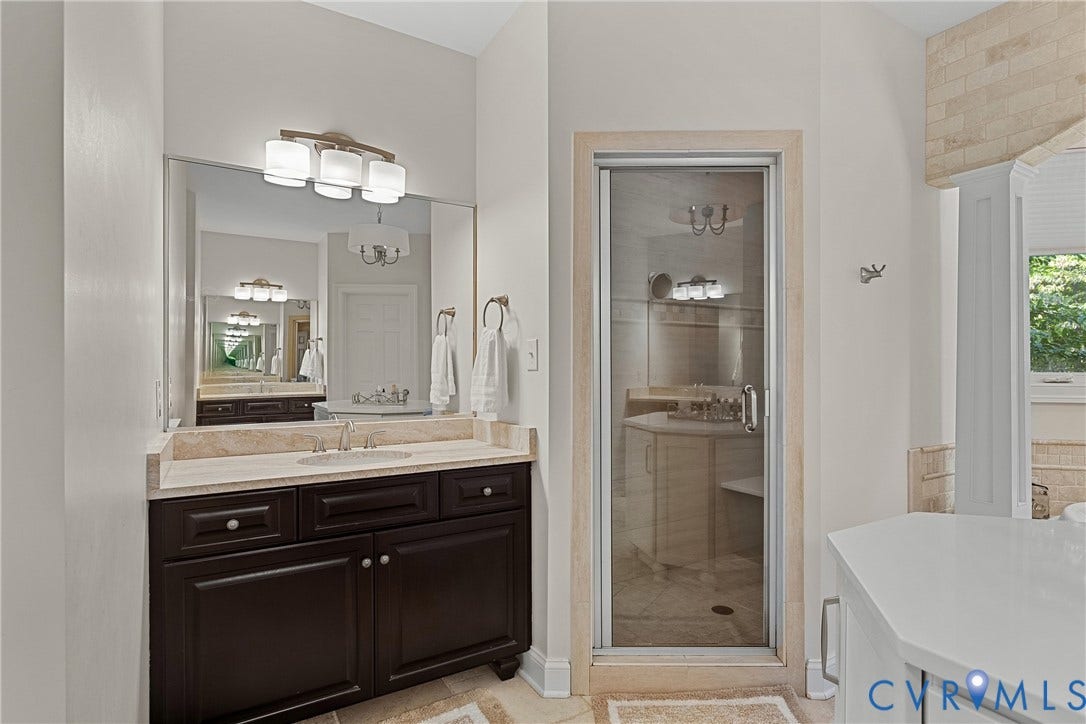 Spa-inspired primary bathroom featuring a dark wood double-vanity with dual sinks, marble countertops, and polished chrome fixtures