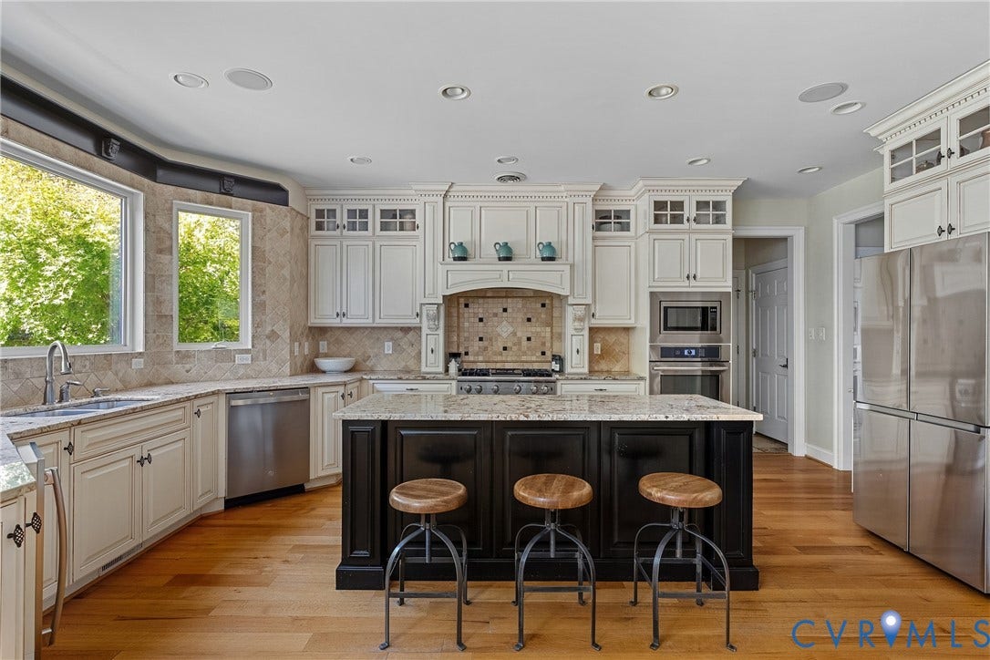 Spacious kitchen featuring an expansive center island, extensive cabinetry with upper glass-front elements, stainless steel appliances, and wood-finish flooring