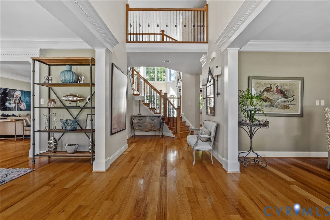 Hardwood flooring throughout the entry, a two-story foyer, a grand staircase with wrought iron balusters, and crown molding details