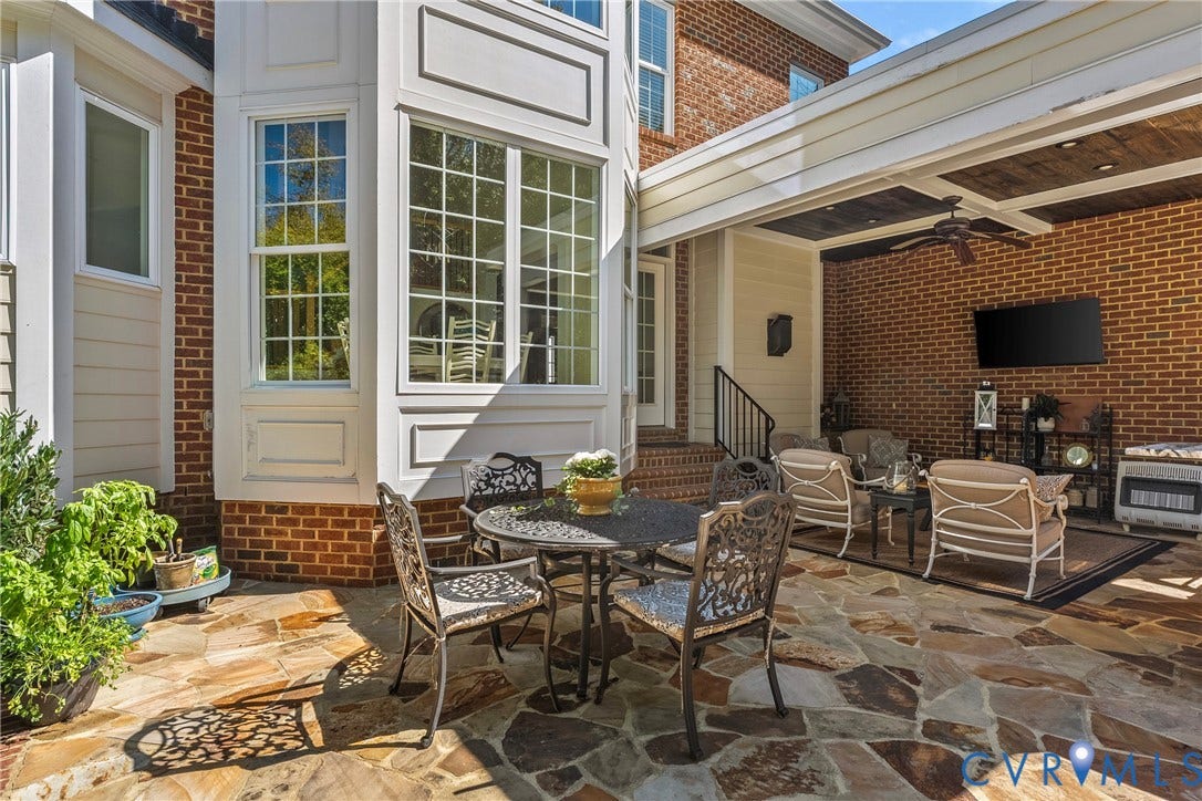 Expansive flagstone patio with a covered outdoor living area, brick exterior, bay window, and a built-in ceiling fan