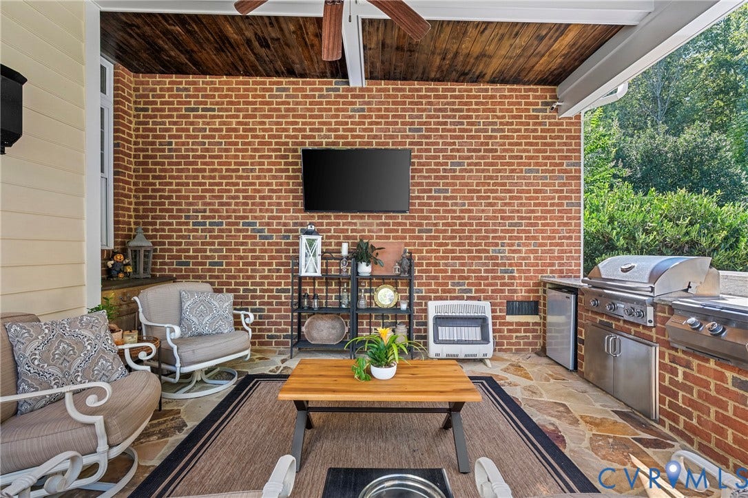 Covered patio featuring a brick accent wall, wood-paneled ceiling, and stone-finish flooring