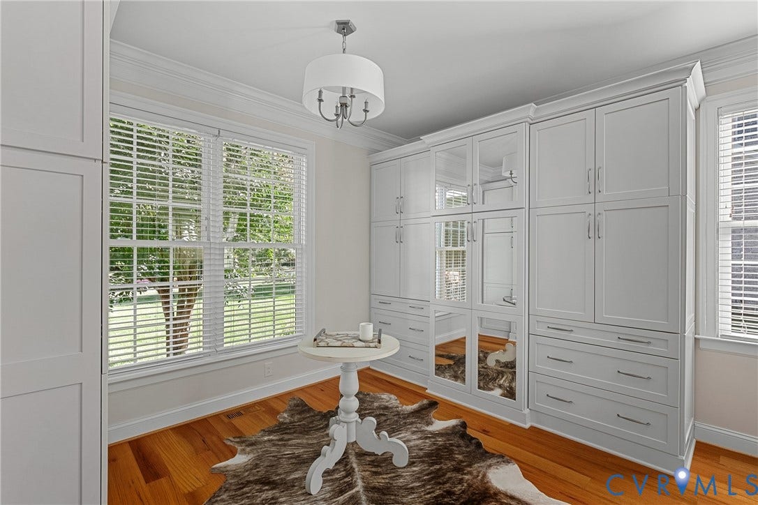 Built-in cabinetry with glass-front and solid panel doors, wood-finish flooring, and a multi-pane window with white blinds