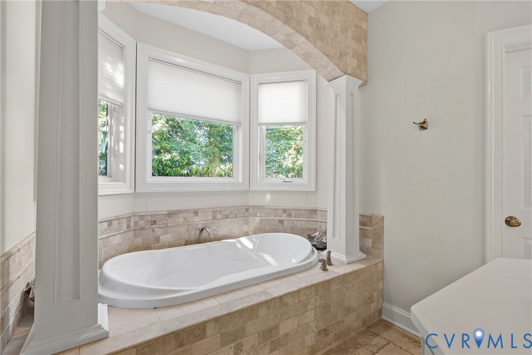 Recessed soaking tub with surrounding tile, arched entryway, and multiple windows