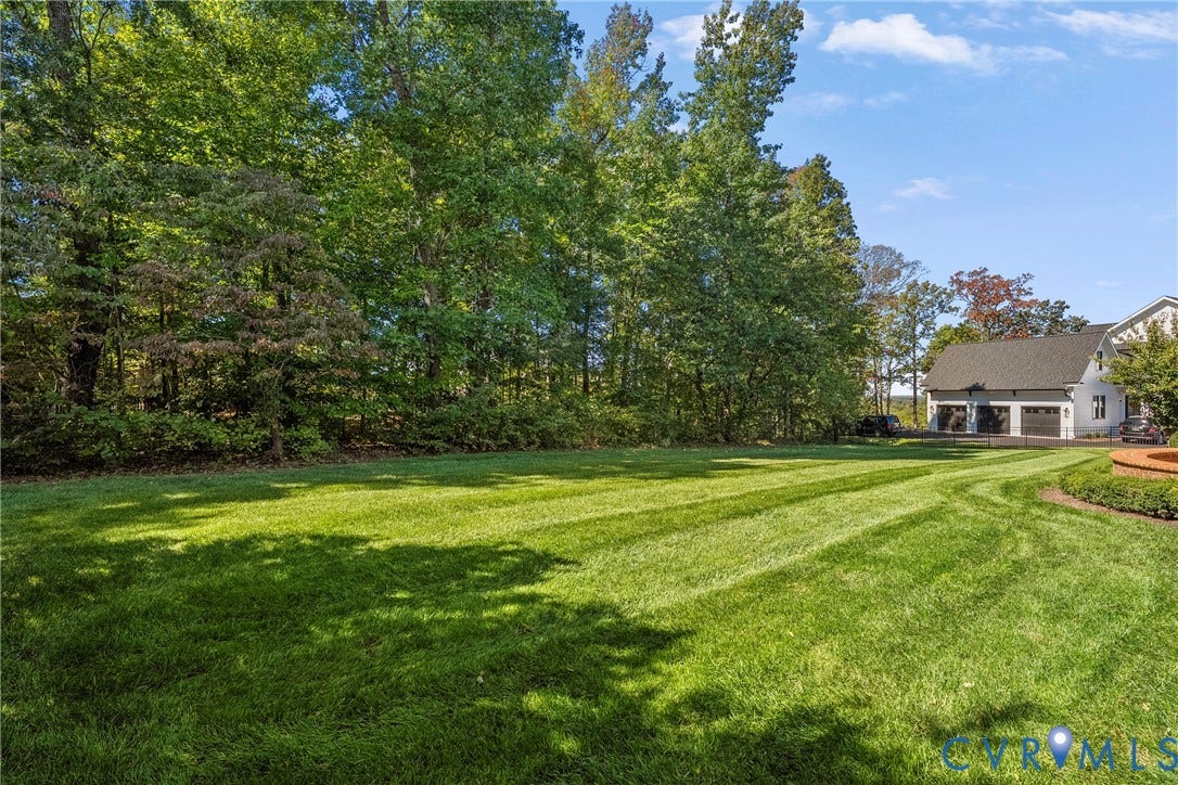 Expansive lawn bordered by mature trees, featuring a garage with three bays and a paved driveway