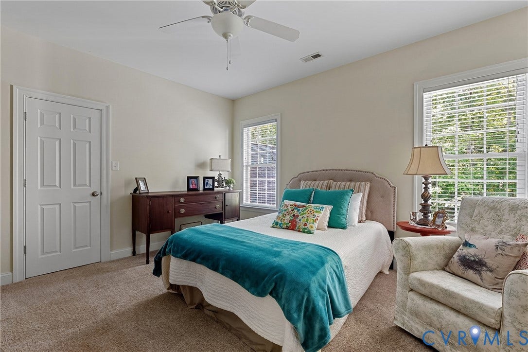 Carpeted room featuring a white ceiling fan with light kit, two windows with blinds, a paneled interior door, and light-toned walls