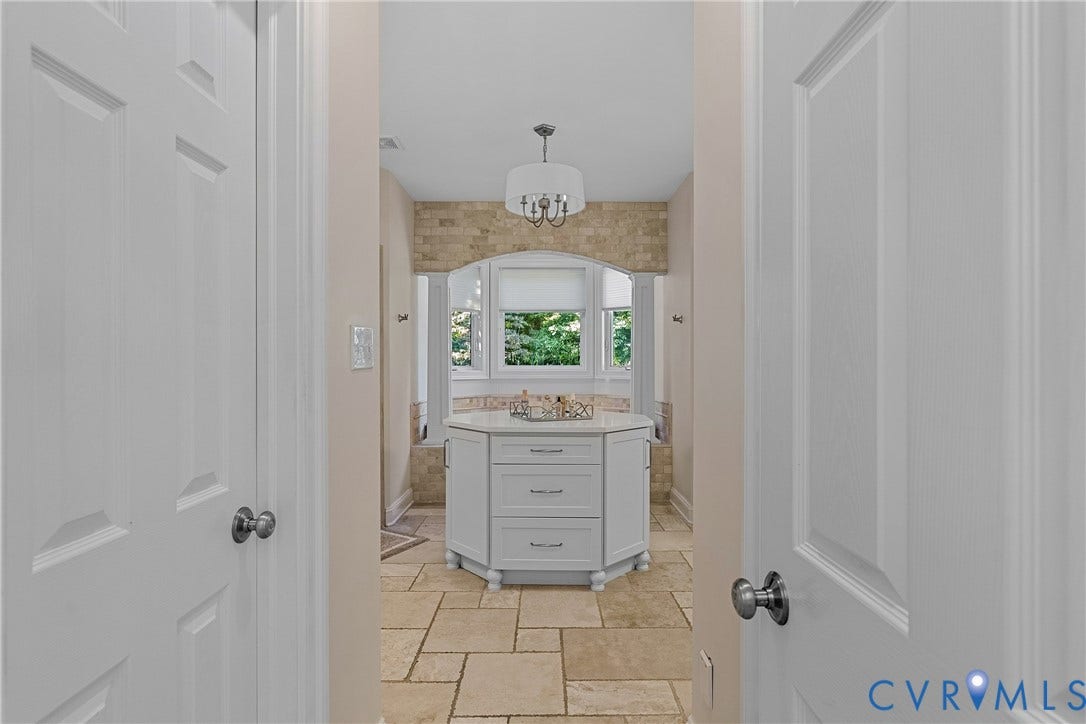 Tiled flooring, freestanding central cabinet with drawers, bay window, built-in bathtub, and overhead light fixture