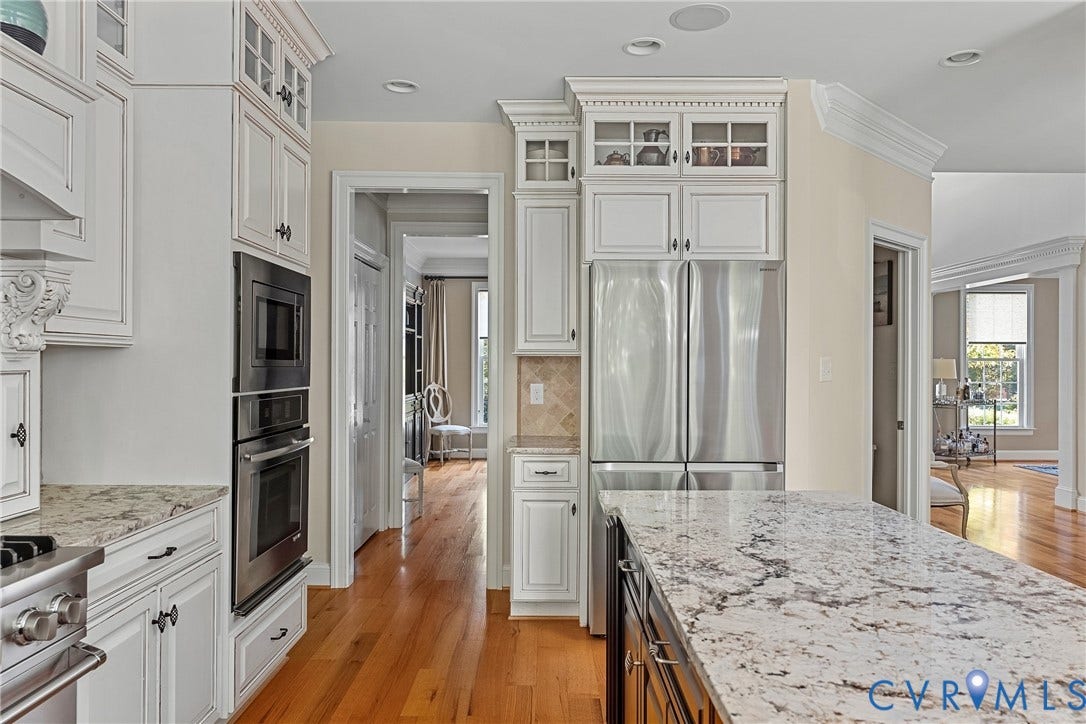 White cabinetry with glass-front accents, stainless steel built-in appliances, light-toned stone countertops, hardwood flooring, and recessed lighting