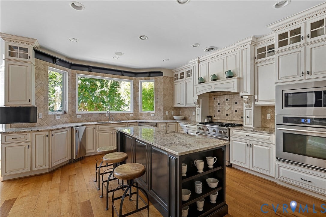 Hardwood flooring, custom cabinetry with glass-front accents, stainless steel appliances, granite countertops, and a tiled backsplash