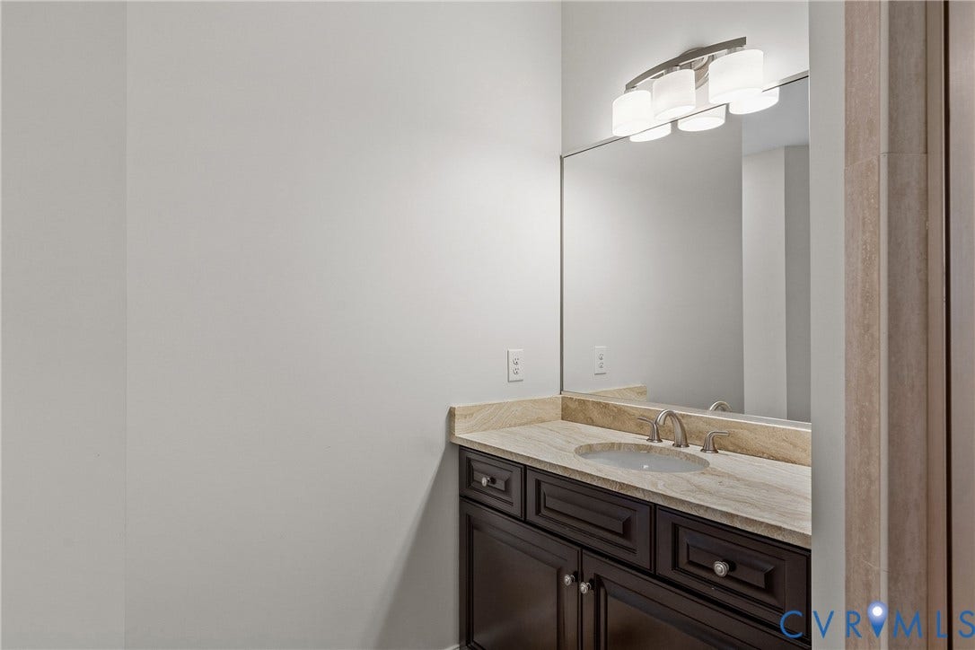 Built-in vanity with a stone countertop, undermount sink, and brushed nickel faucet