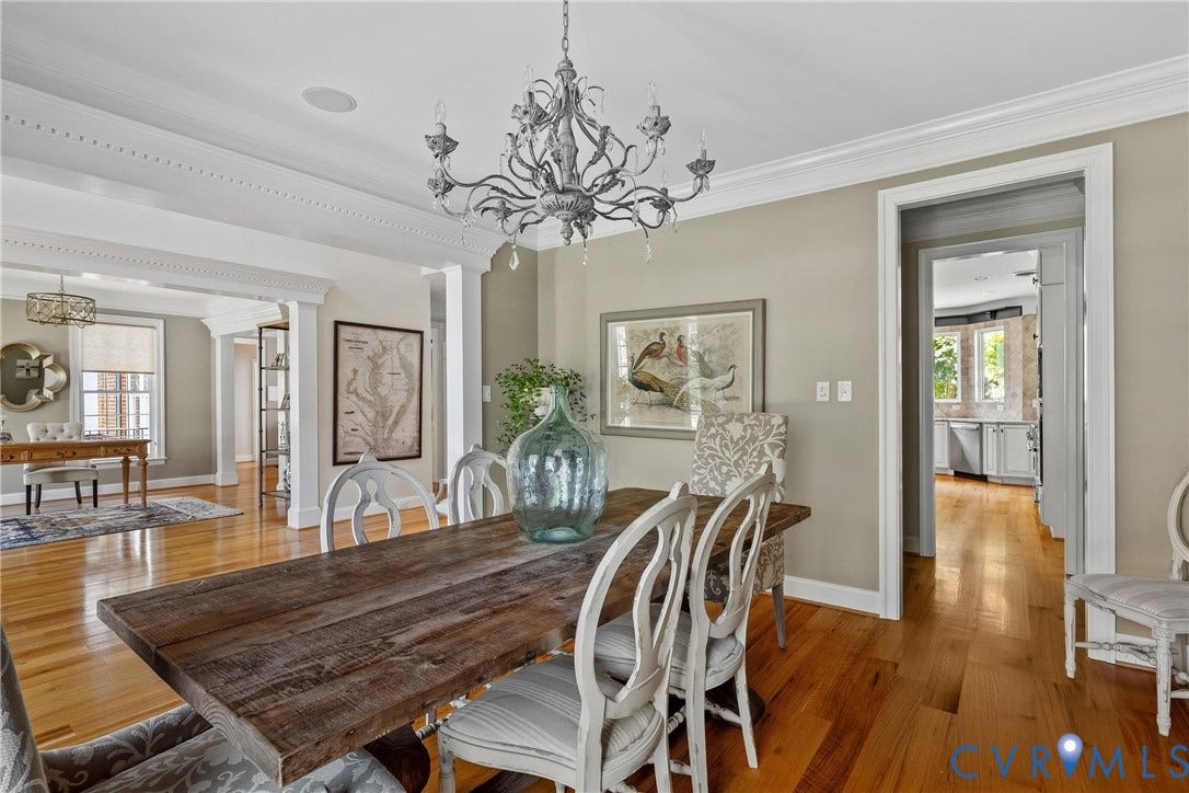 Hardwood flooring, decorative crown molding, recessed lighting, and a chandelier illuminate this dining area