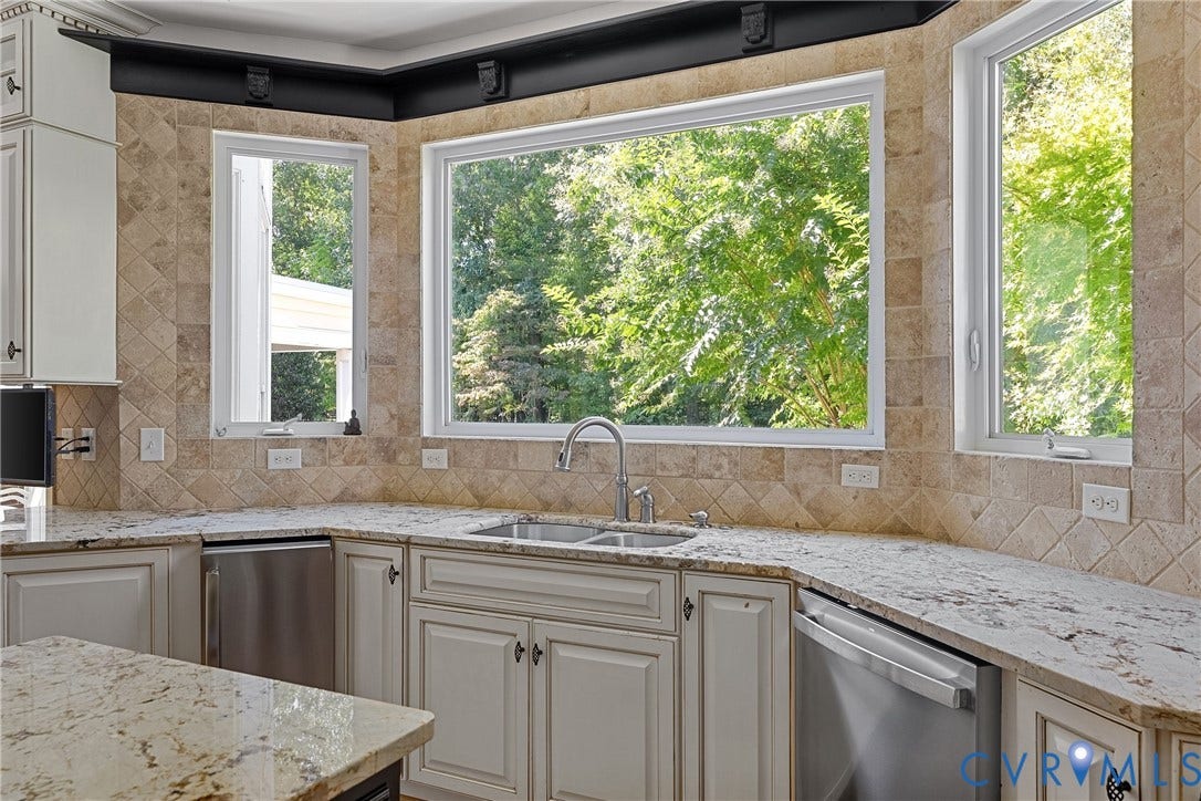 Bay window with undermount sink, dual stainless steel appliances, light-toned cabinetry, and stone countertops