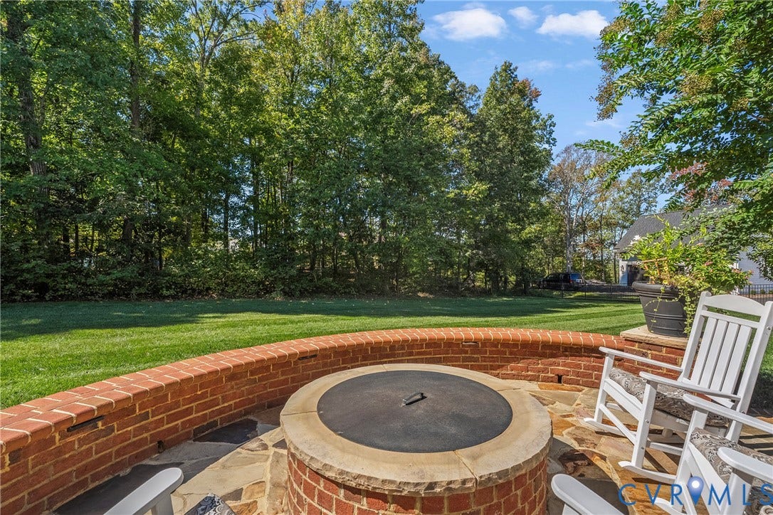 Stone patio featuring a built-in brick fire pit with a stone cap, surrounded by a curved brick wall and a manicured lawn
