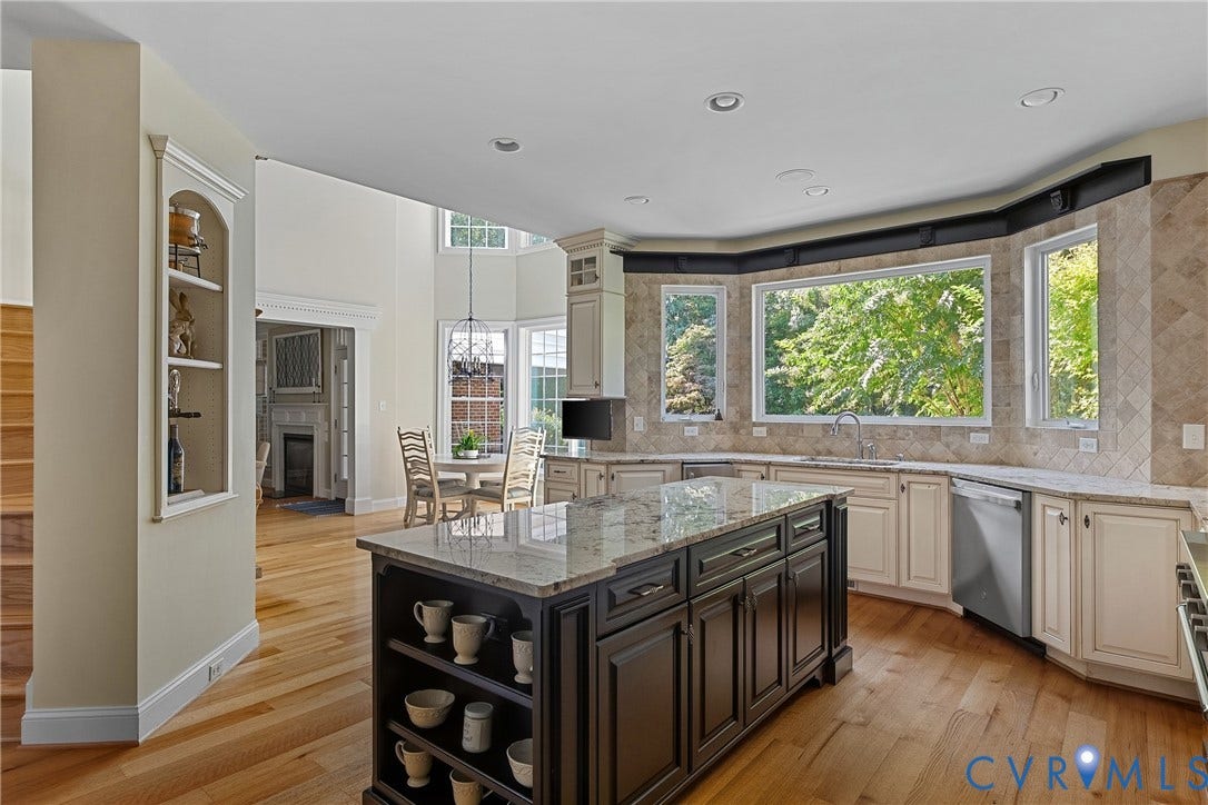 Spacious kitchen featuring a large central island with granite countertop, abundant cabinetry, and a tile backsplash
