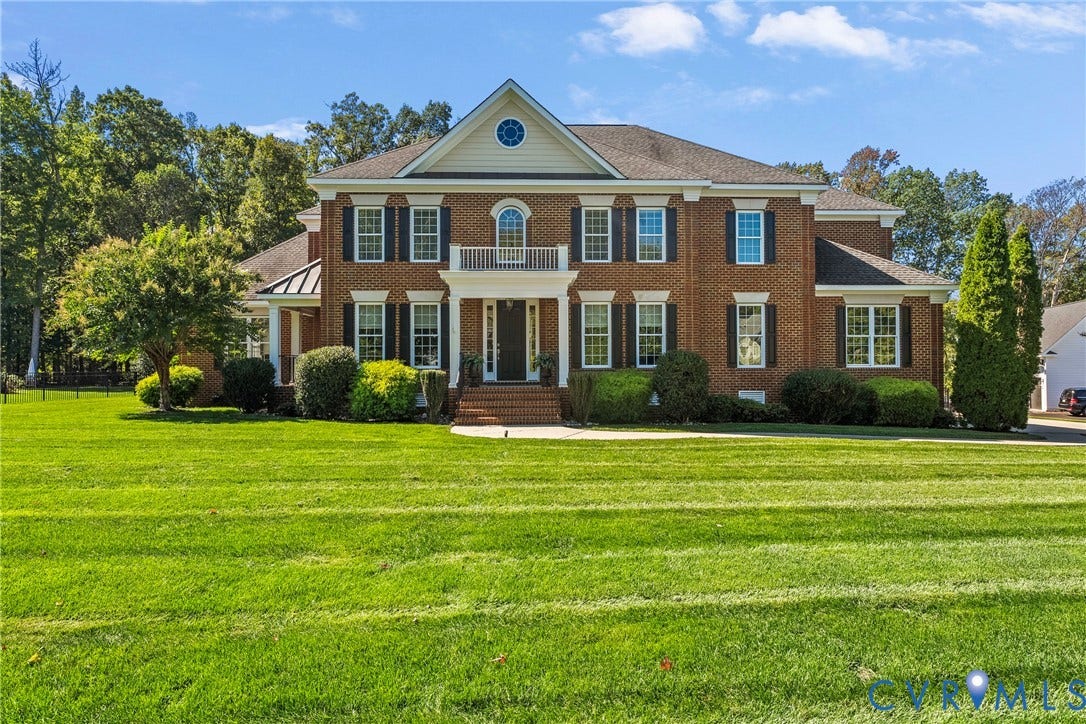Traditional brick exterior with white trim, featuring a prominent front entrance with columns, a second-story balcony, and a circular window accent