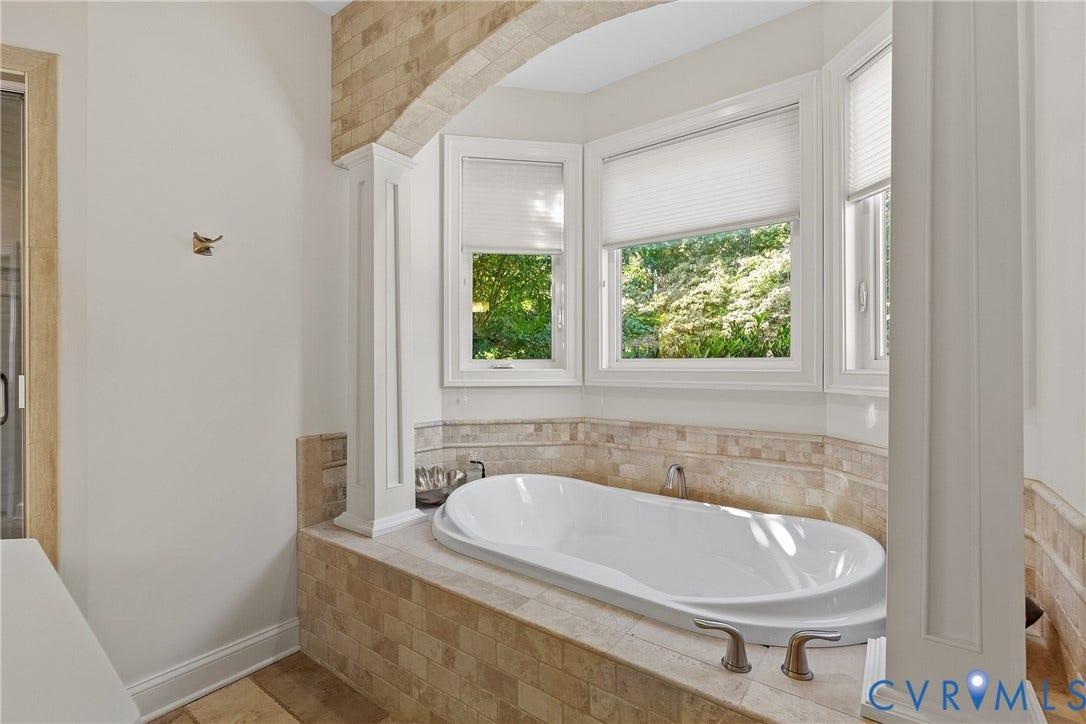 Built-in soaking tub with brushed nickel fixtures, surrounded by tiled decking and a bay window