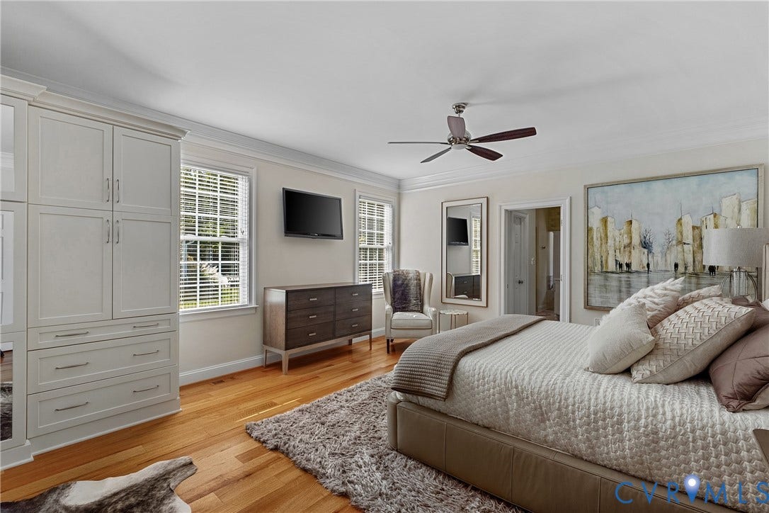 Warm wood-finish flooring, built-in cabinetry, dual windows with blinds, a ceiling fan, and crown molding