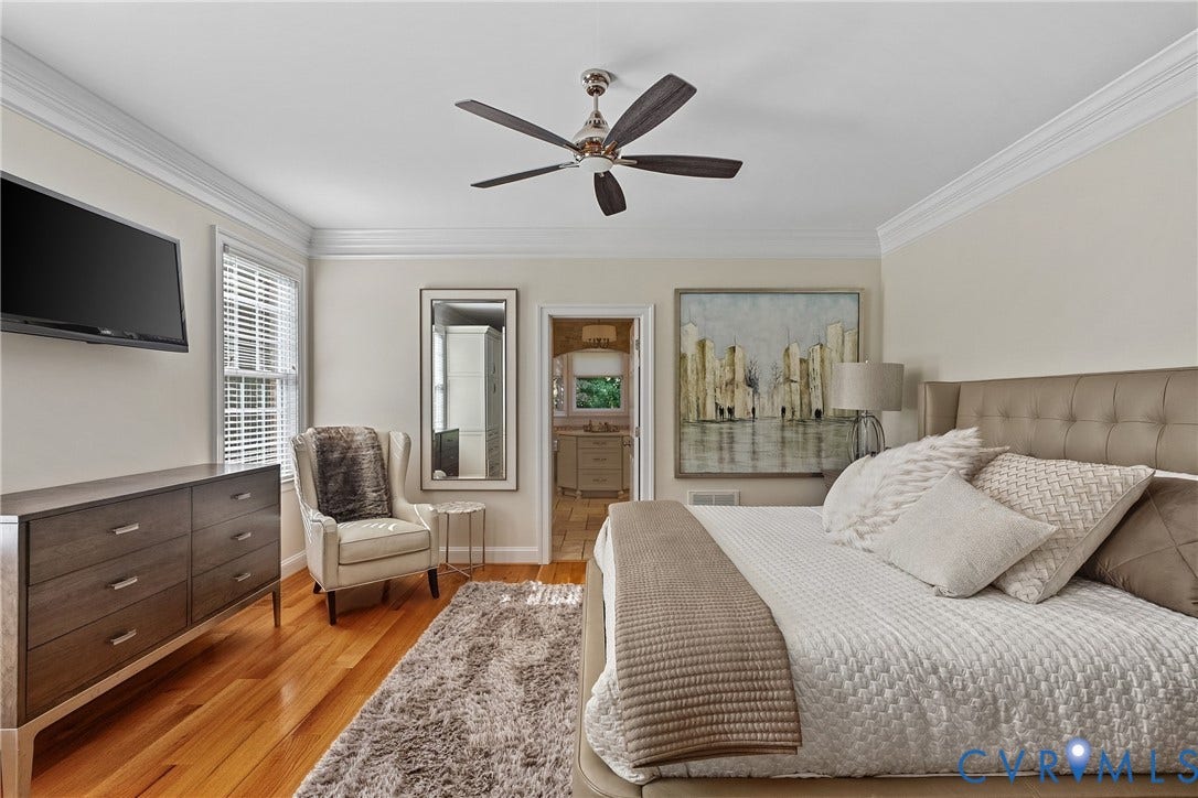Hardwood flooring, crown molding, ceiling fan, tufted upholstered headboard, and a built-in window with blinds