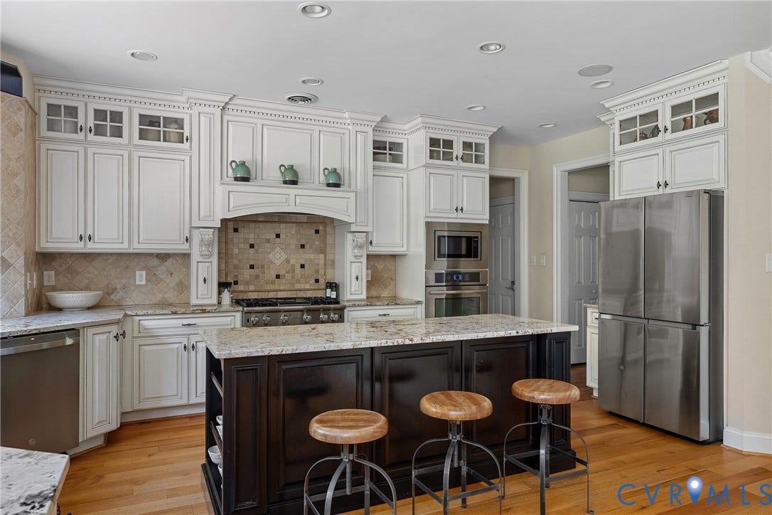 Gourmet kitchen featuring white cabinetry, a large kitchen island with a light-toned countertop, stainless steel appliances, and wood-finish flooring