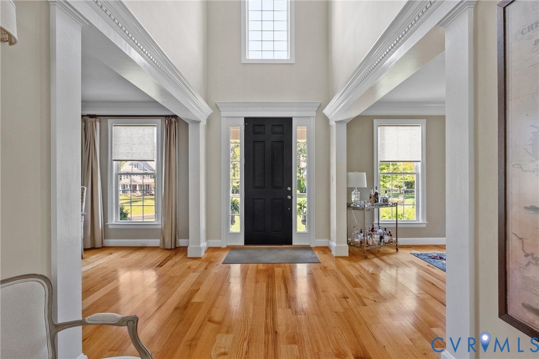 Two-story entryway featuring wood-finish flooring, a dark paneled door with sidelights, and an overhead transom window