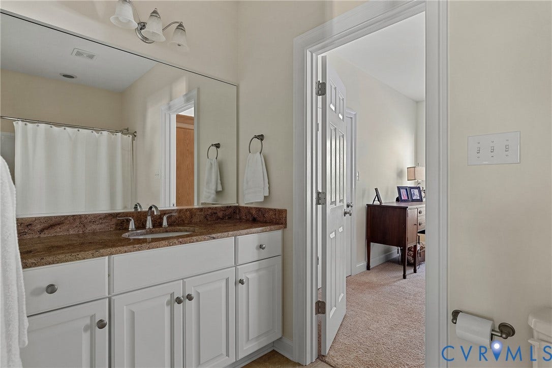 Bathroom vanity featuring a brown countertop, white cabinetry with round hardware, and a large wall-mounted mirror