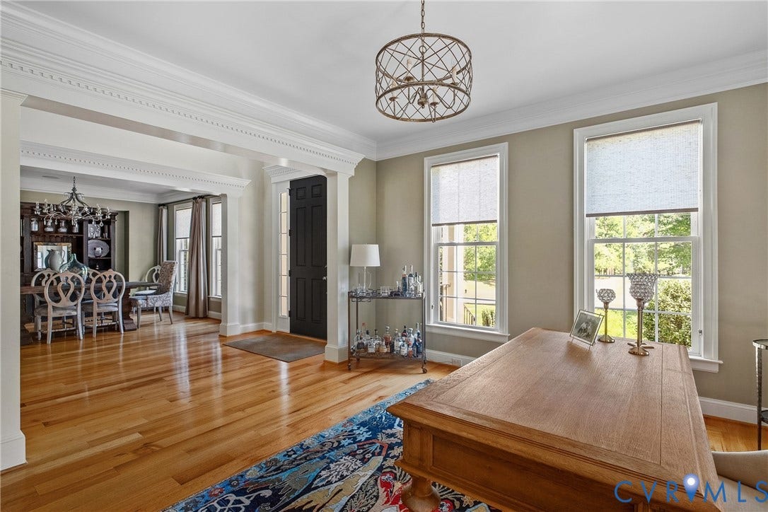 Hardwood flooring throughout, elegant crown molding, decorative chandelier, and a black paneled door