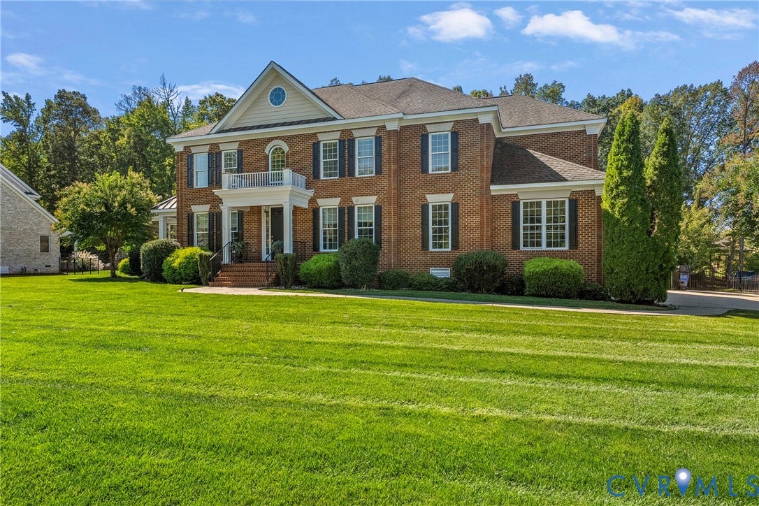 Brick exterior with contrasting dark shutters, a prominent front portico, second-story balcony, and a gable dormer