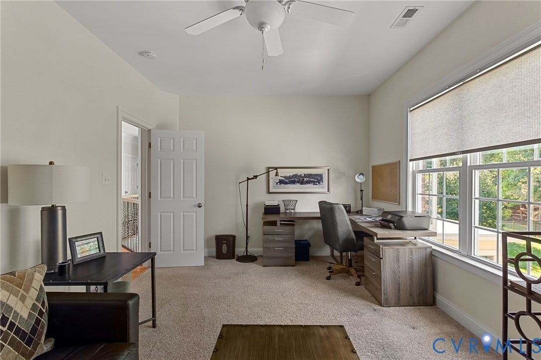 Carpeted room with a ceiling fan, large window with roller shades, and a paneled door
