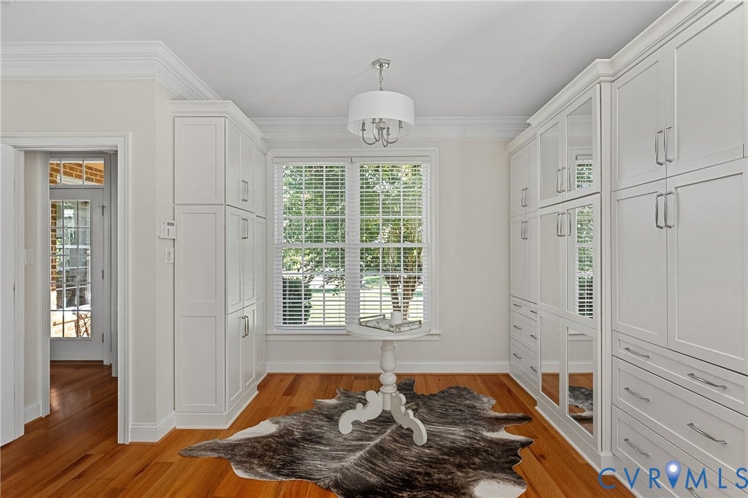 Hardwood flooring, extensive white built-in cabinetry, window with white blinds, recessed lighting, and a white chandelier